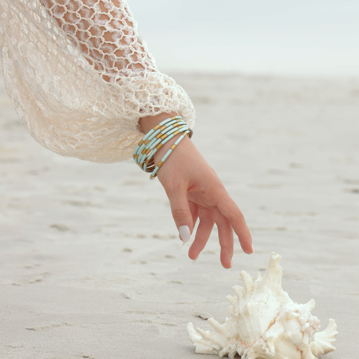 a hand reaching for a shell on a beach